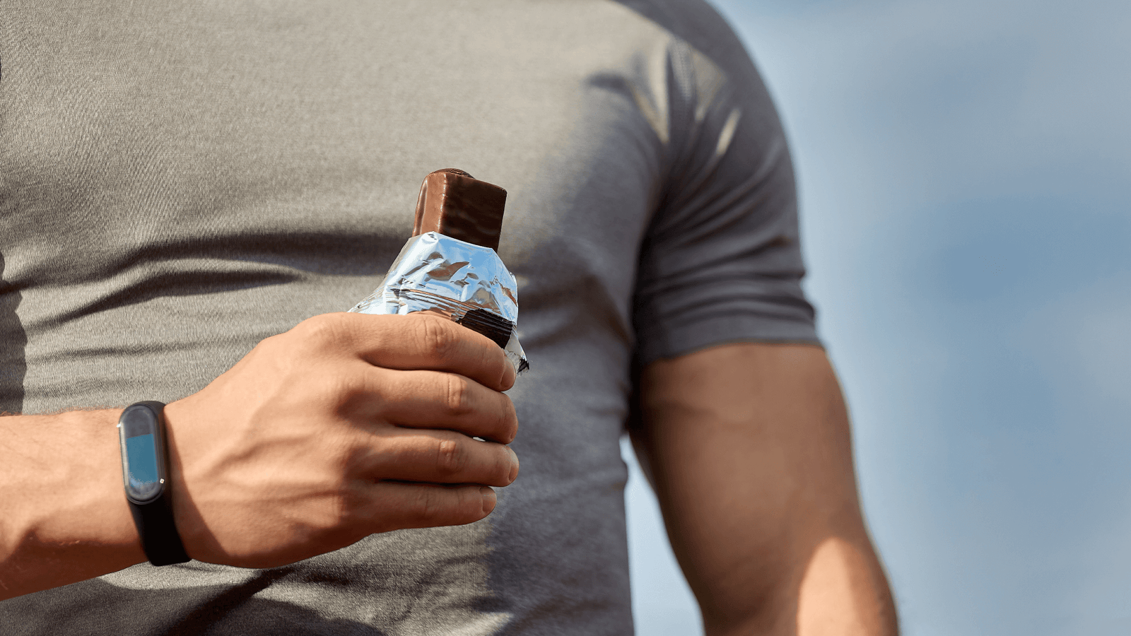 A man in a gray short holding an opened candy bar.