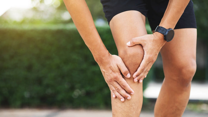 A person wearing athletic clothing holds their knee with both hands, indicating discomfort or pain, suggesting a possible sports-related injury.