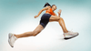 Woman in athletic wear mid-stride, running against a light blue background, captured from a low-angle perspective.