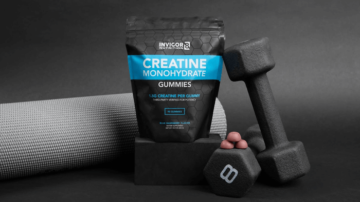 A bag of Invigor8 Creatine Gummies beside dumbbells and a yoga mat.