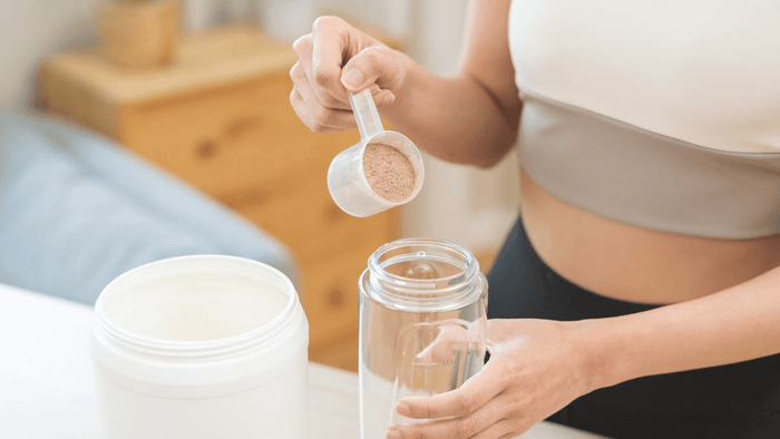 Person scooping protein powder into a blender bottle.