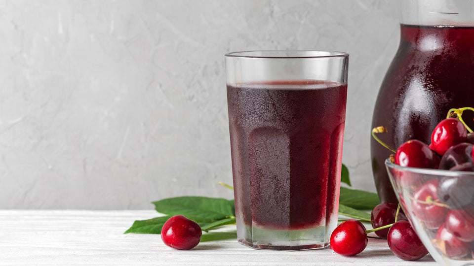 image of a cup of cherry juice with a pitcher and a bowl of fresh cherries