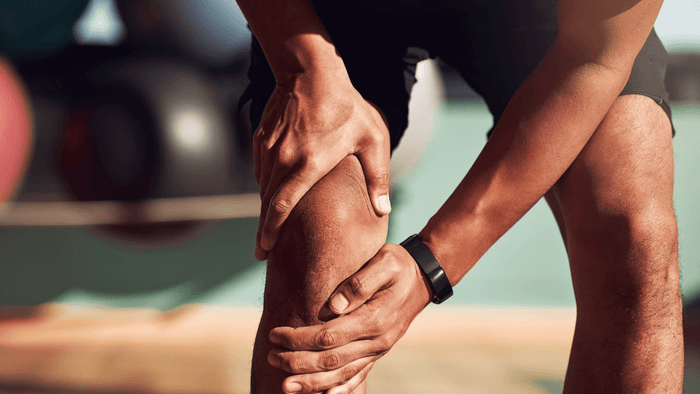 A person gripping their knee in a gym, suggesting knee pain or injury.